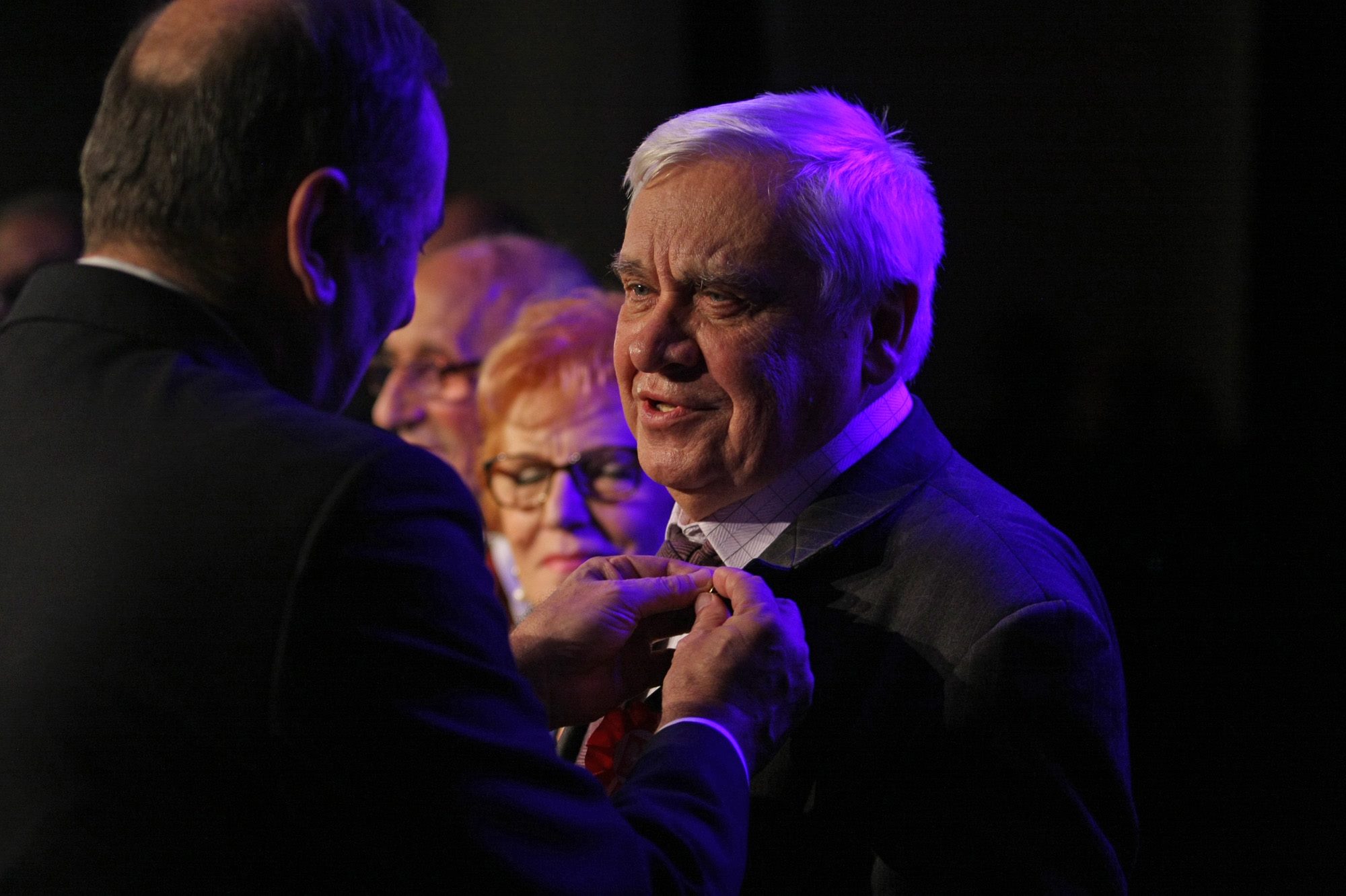 Profesor Kazimierz Kozłowski w chwili otrzymywania tytułu Honorowego Obywatela Świnoujścia. Na pierwszym planie moment przypinania odznaczenia, w tle widoczni uczestnicy uroczystości.